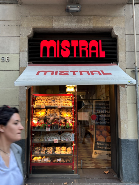 Bakery storefront with many goods displayed. Sign in bright neon orange says "MISTRAL."